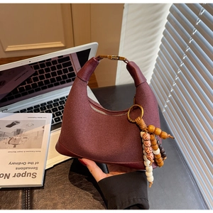 Détail du sac hobo bordeaux à texture mate avec breloque décorative à pompon perlé