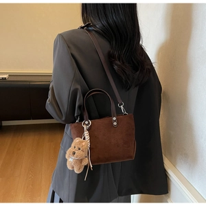 Dettaglio borsa a secchiello scamosciata marrone con ciondolo teddy su blazer grigio