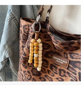 Close-up of leopard print tote bag featuring wooden bead charm and leather brand tag