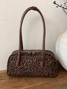 Retro leopard print baguette shoulder bag with leather handles on a rustic wooden surface