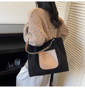 Detail of large tote bag showing leather pocket with embossed logo and metal chain strap