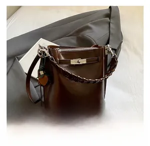 Detail of dark brown bucket bag with woven handle and orange charm on white bedding