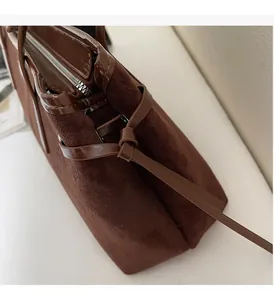 Detail view of dark brown suede and patent leather handbag with silver zipper and knot accents