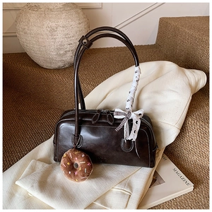 Détail du sac baguette en cuir marron foncé avec nœud en dentelle et pendentif donut