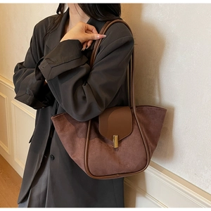 Detail of a brown suede and leather bucket bag featuring a rectangular gold metal buckle