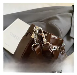 Detail of silver polished metal hook and wide woven leather strap on brown bucket bag