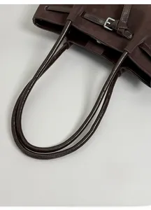 Detail of dark brown tote bag with matte finish, glossy handles, and silver metal buckle