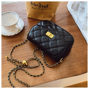 Detail of black quilted leather crossbody bag with golden chain and clasp on wooden table