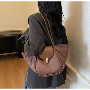 Close-up of brown suede tote bag with leather trim and gold metal clasp on model