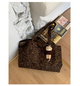 Detail of leopard print tote bag with brown bear keychain on a white sofa backdrop