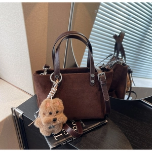Dettaglio ravvicinato di borsa tote in pelle scamosciata marrone con ciondolo a peluche