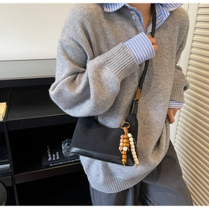Détail d'un sac baguette en toile noire et cuir avec un pendentif en perles style folk