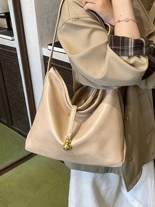 Sac hobo minimaliste en cuir beige avec pendentif doré porté à l'épaule par un mannequin