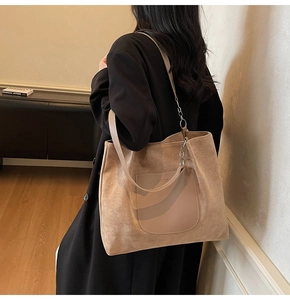 Close-up of tan suede tote bag with leather pocket and silver chain strap on model