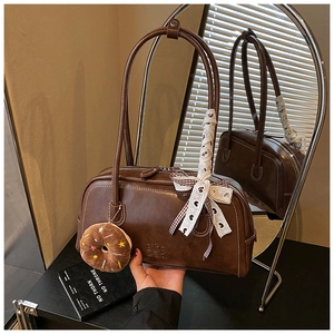 Détail du sac baguette marron avec ruban en dentelle et breloque donut sur un miroir