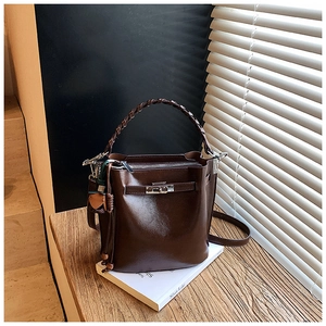 Detail of dark brown bucket bag featuring woven handle and metal twist lock closure
