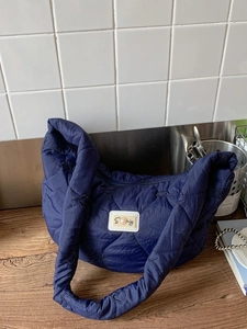 Quilted navy blue hobo bag with heart patterns and padded handle on a wooden table