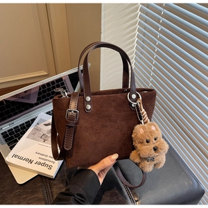 Dettaglio della borsa tote in pelle scamosciata marrone scuro con ciondolo a orsetto