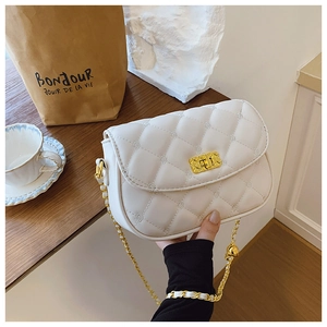 Close-up of white quilted crossbody bag with gold chain strap on a wooden table