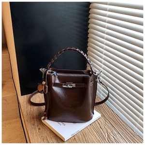Detail of dark brown leather bucket bag with woven handle and metallic clasp closure