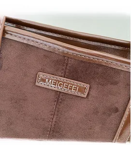 Macro detail of brown suede fabric and shiny leather stitching with logo on handbag