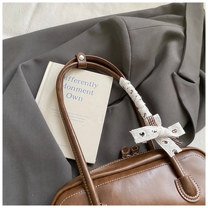 Détail de sac baguette vintage marron avec nœud en dentelle blanche sur la bandoulière