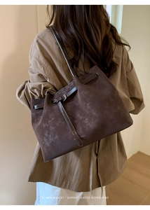 Close-up of a large dark brown suede tote bag carried by a model in a minimalist room