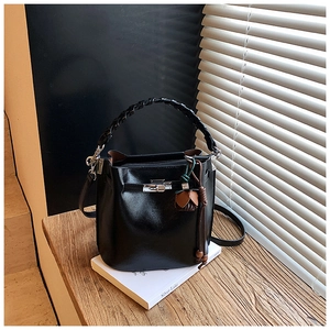 Detail of black glossy bucket bag with woven handle and vintage floral tassel pendant