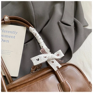 Détail du sac baguette marron vintage avec poignées en dentelle blanche et nœud à carreaux