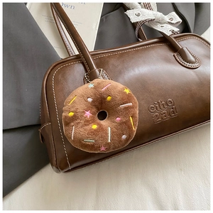 Détail d'un charme en peluche de beignet au chocolat brodé sur un sac en cuir chic