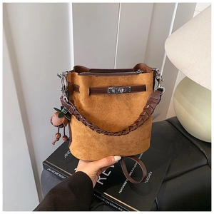 Detail of warm brown suede bucket bag with woven handle and strawberry charm