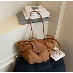 Detail of a brown suede and leather tote bag with a minimalist metal clasp and long straps