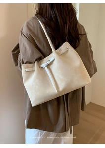Model wearing a large cream suede tote bag with buckle detail in a minimalist setting