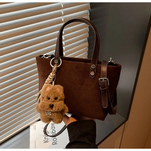 Dettaglio della borsa a secchiello in camoscio marrone con manico in pelle e ciondolo