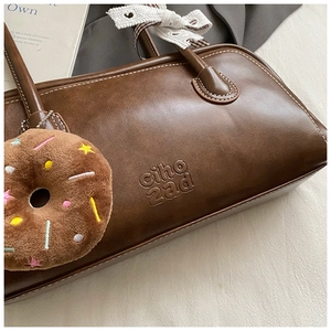 Détail du sac baguette marron avec surpiqûres blanches et nœud en dentelle