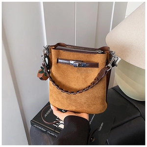 Detail of a brown suede bucket bag featuring a woven handle and leaf-shaped charm
