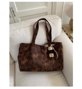 Detail of large leopard print tote bag with plush bear charm on white fabric sofa