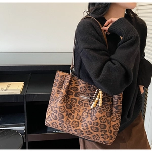 Close-up of leopard print tote bag featuring a leather logo tag and wooden bead charm