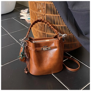 Detail of a brown leather bucket bag featuring a woven handle and metallic swivel lock
