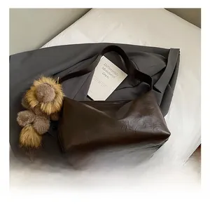 Détail du grand sac cabas en cuir marron foncé avec breloque peluche sur un blazer