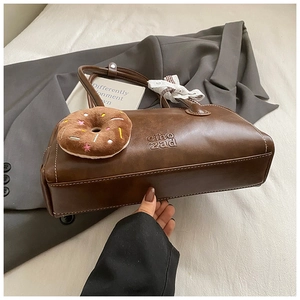 Détail du sac baguette en cuir mat marron foncé avec logo embossé et breloque donut en peluche
