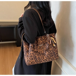Detail of leopard print tote bag featuring a beaded tassel charm and brown leather straps