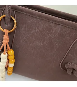 Detail of dark brown tote bag with vintage texture, gold logo and beaded ring charm
