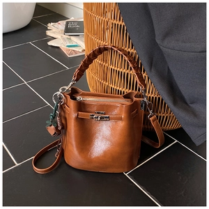 Detail of brown glossy leather bucket bag with woven handle and metal buckle on chairs