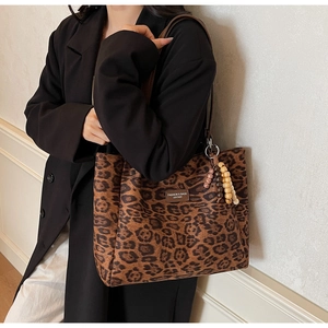 Close-up of leopard print tote bag with brown leather label and beaded keychain detail