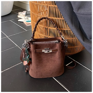 Detail of a brown suede bucket bag with woven handle, silver lock, and strawberry charm