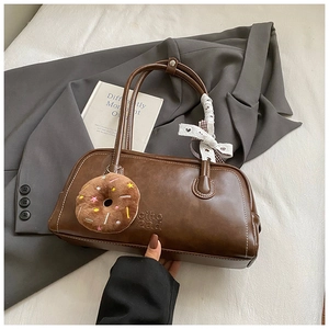 Détail du sac baguette marron foncé avec logo embossé et breloque donut en peluche