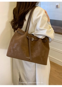 Detail of a large brown suede tote bag featuring a decorative metal buckle and slim strap