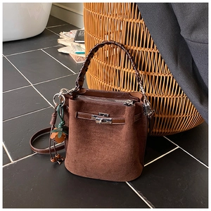 Detail of brown suede bucket bag with leather woven handle and strawberry charm