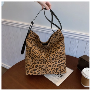 Detail view of large leopard print hobo bag with black leather straps on a wooden table